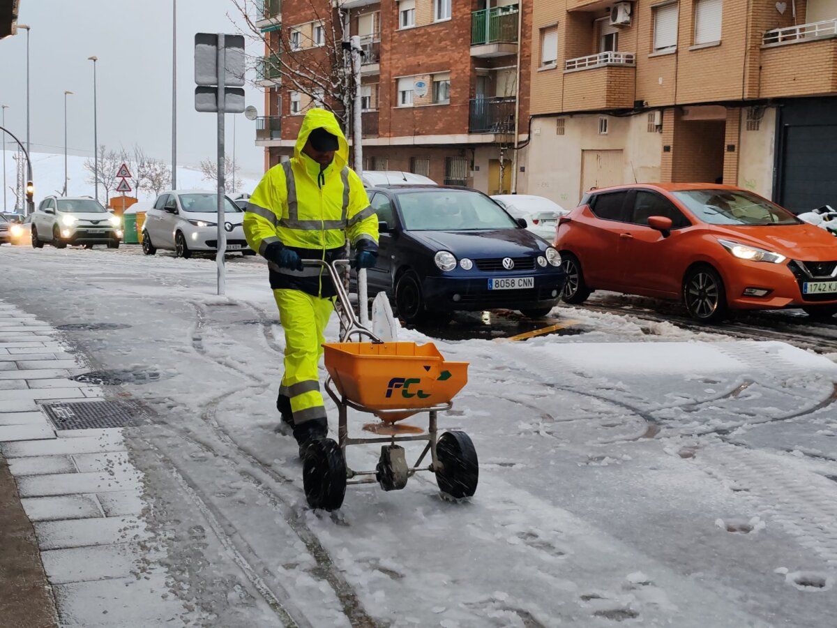 Trabajador en chaqueta amarilla esparciendo sal en una calle nevada