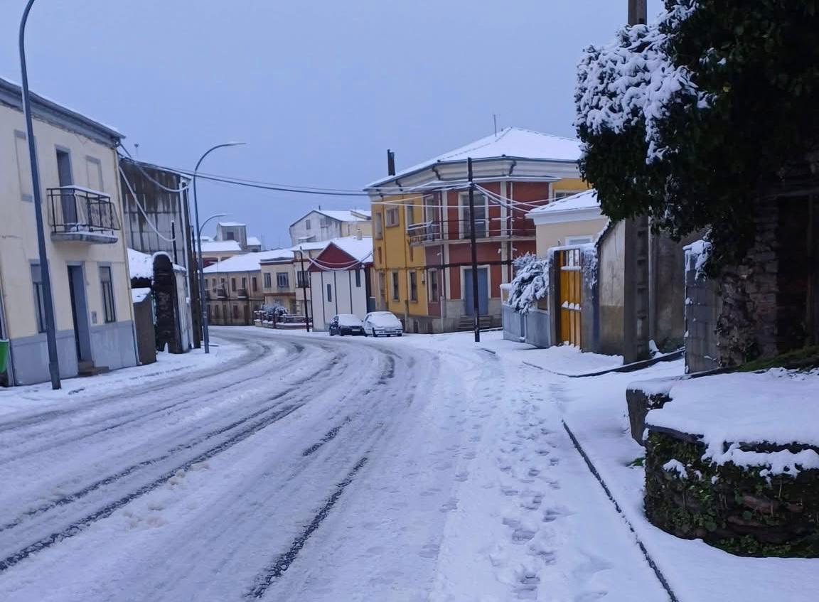 Calle nevada en Guijuelo con edificios y vehículos cubiertos de nieve