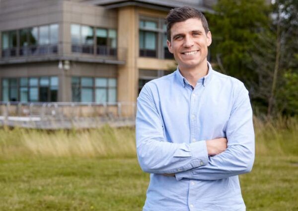 Íñigo Martincorena sonriente en un entorno natural con un edificio moderno al fondo