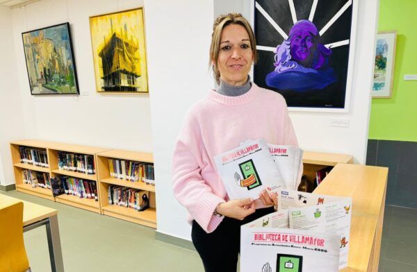Mujer sosteniendo folletos de programación cultural en la biblioteca de Villamayor