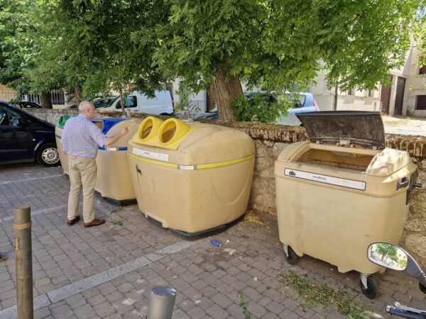 Persona separando residuos en contenedores de reciclaje en la calle.