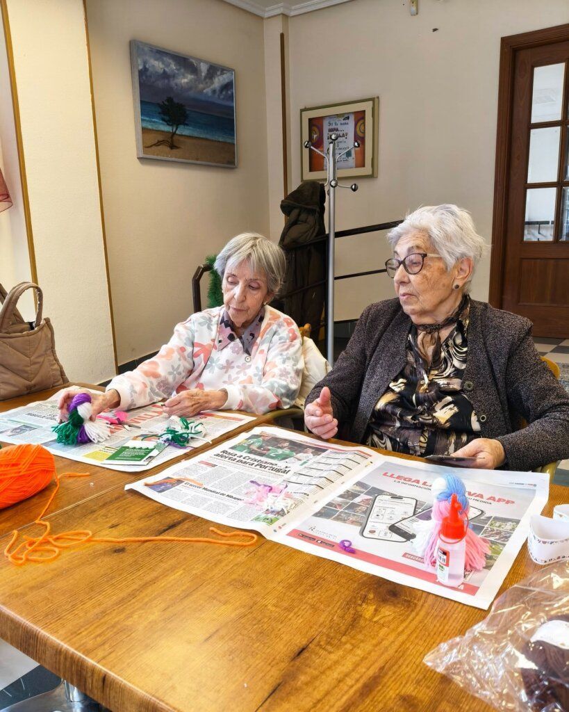 Dos mujeres mayores participan en un taller creativo con materiales de manualidades.