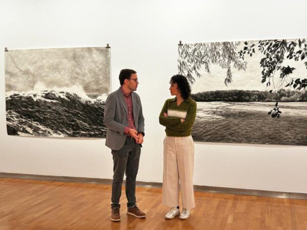Dos personas conversando en una galería de arte con obras de Gabriela Bettini.