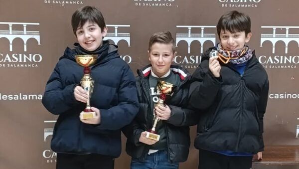 Tres jóvenes ajedrecistas sosteniendo trofeos en el Casino de Salamanca