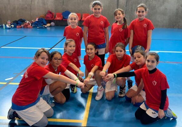 Grupo de niñas en camisetas rojas mostrando brazaletes verdes en un gimnasio
