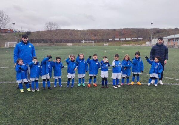 Niños en un campo de fútbol con chaquetas azules levantando el brazo