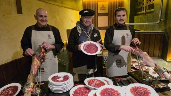 Tres hombres en la Matanza de Carnaval en Guijuelo, mostrando platos de jamón ibérico.