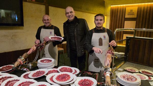 Tres hombres presentan platos de jamón ibérico en la Matanza de Carnaval en Guijuelo.