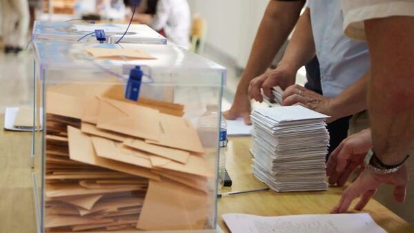 Mesa electoral con votos y personas contando papeletas