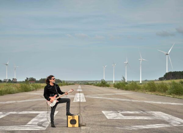 Quique González tocando la guitarra en un paisaje abierto con molinos de viento