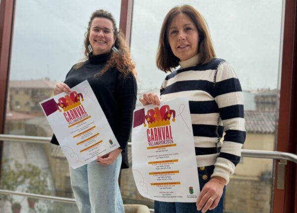 Dos mujeres sosteniendo carteles del Concurso de Disfraces del Carnaval 2026 en Villamayor.