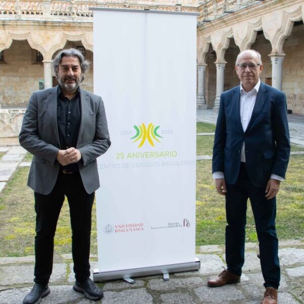 Dos hombres posando junto a un cartel del 25 aniversario del Centro de Estudios Brasileños.