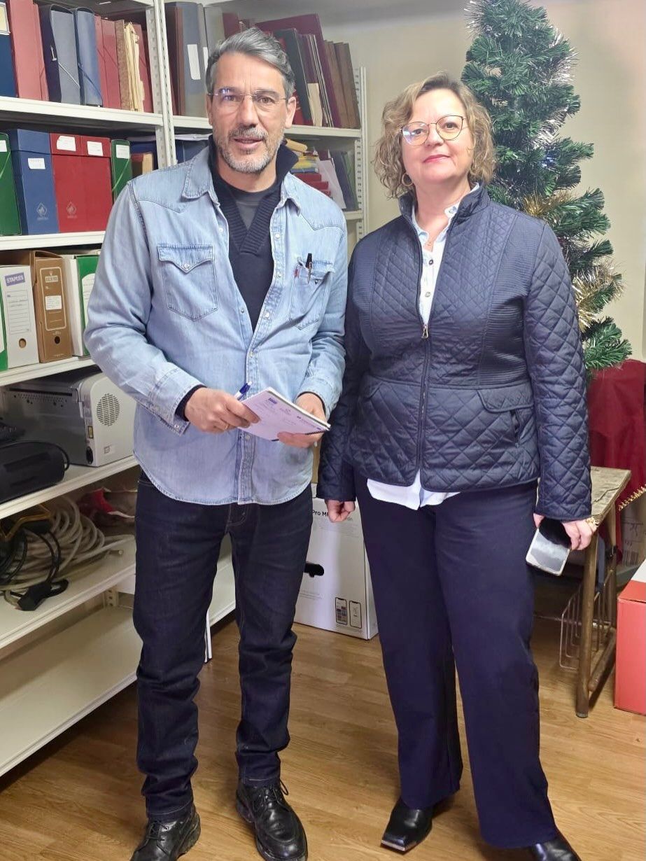 Dos personas en una oficina con archivos y un árbol decorativo
