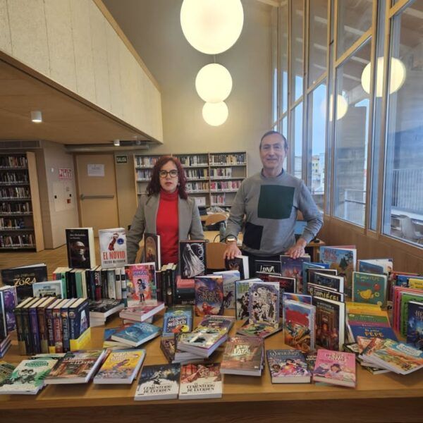 Dos personas en una biblioteca junto a una mesa llena de libros nuevos