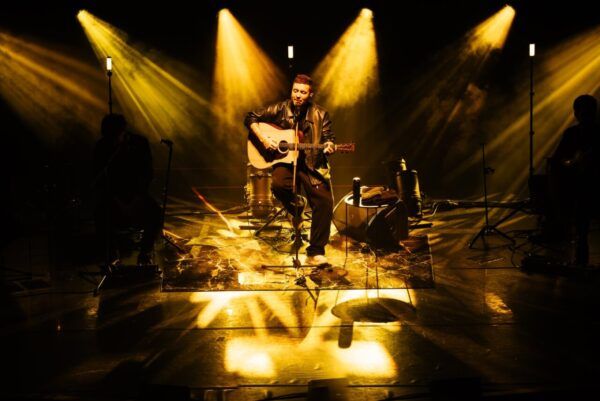 Artista Beret tocando la guitarra en un escenario iluminado