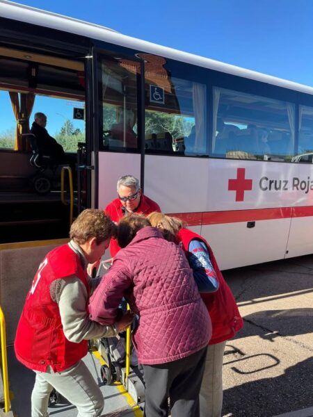 Voluntarios de Cruz Roja ayudan a votantes con movilidad reducida a subir a un autobús adaptado.