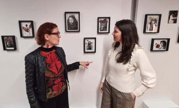 Dos mujeres conversando frente a retratos en la exposición Ancestras/Maestras.