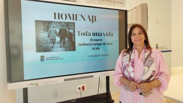 Mujer sonriente junto a un cartel del homenaje Toda una vida en Santa Marta