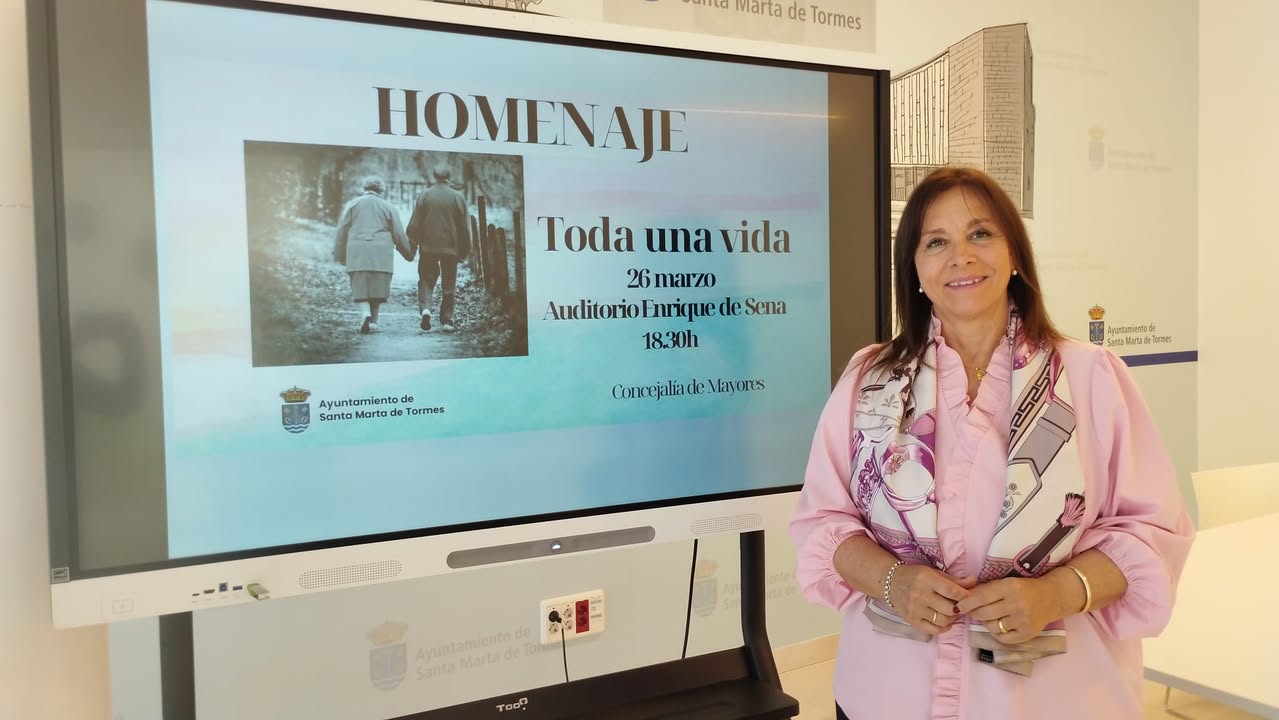 Mujer sonriente junto a un cartel del homenaje Toda una vida en Santa Marta