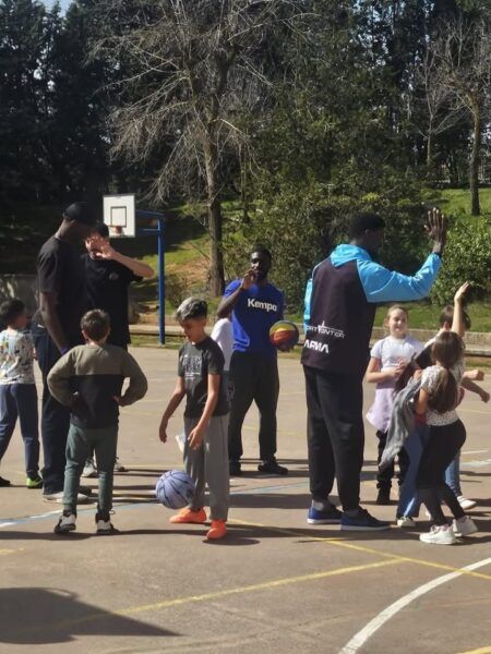Jugadores de baloncesto interactuando con niños en el patio del colegio
