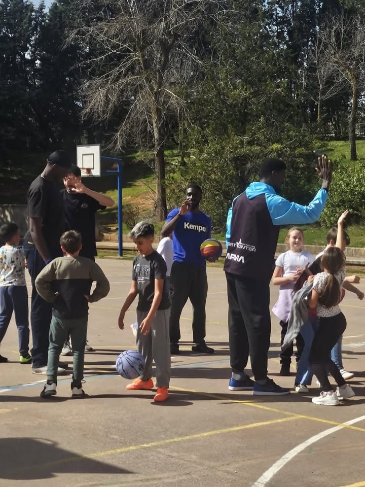 Jugadores de baloncesto interactuando con niños en el patio del colegio