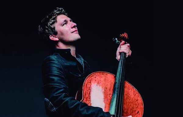 Violonchelista Maximilian Hornun sosteniendo su instrumento en un escenario oscuro