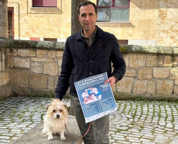 Hombre sosteniendo un cartel del VI Canicross Fundación Luna con un perro