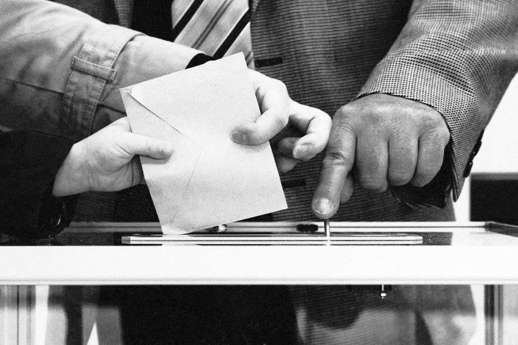 Manos de un adulto y un niño depositando un voto en una urna