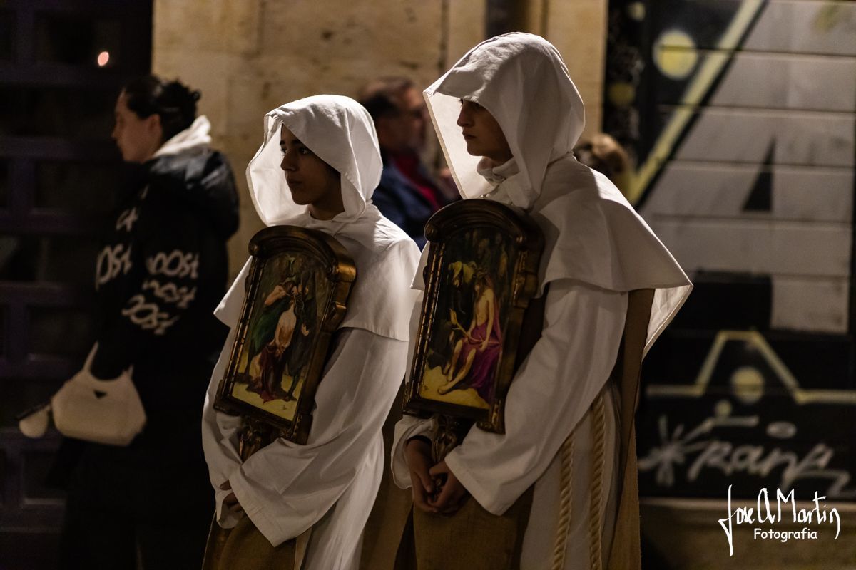 Dos personas con túnicas blancas sosteniendo imágenes religiosas durante la Semana Santa.