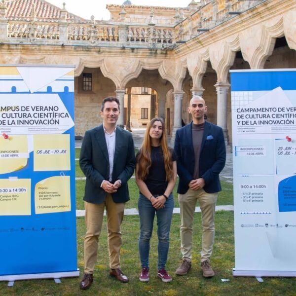 Tres personas posando frente a un cartel del campamento de verano de ciencia.