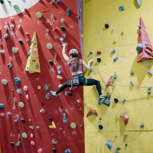 Mujer escalando en un rocódromo con paredes de colores