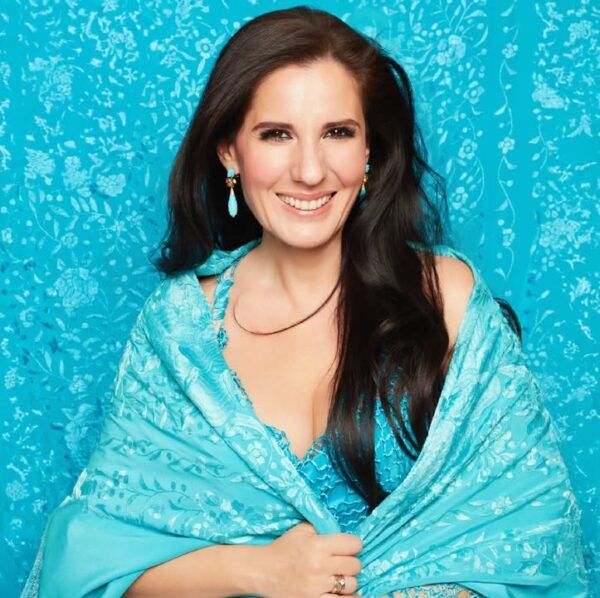 Diana Navarro sonriente con un chal azul en un fondo decorativo