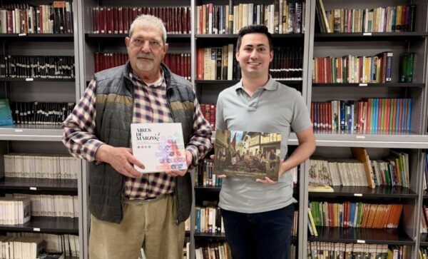 Dos hombres sosteniendo libros en una biblioteca municipal