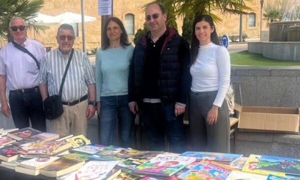 Grupo de personas en un mercadillo solidario de libros con mesas llenas de libros.
