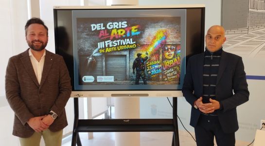 Dos hombres junto a una pantalla que anuncia un festival de arte urbano