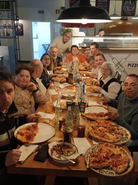 Grupo de personas disfrutando de una comida en una mesa con pizzas y bebidas