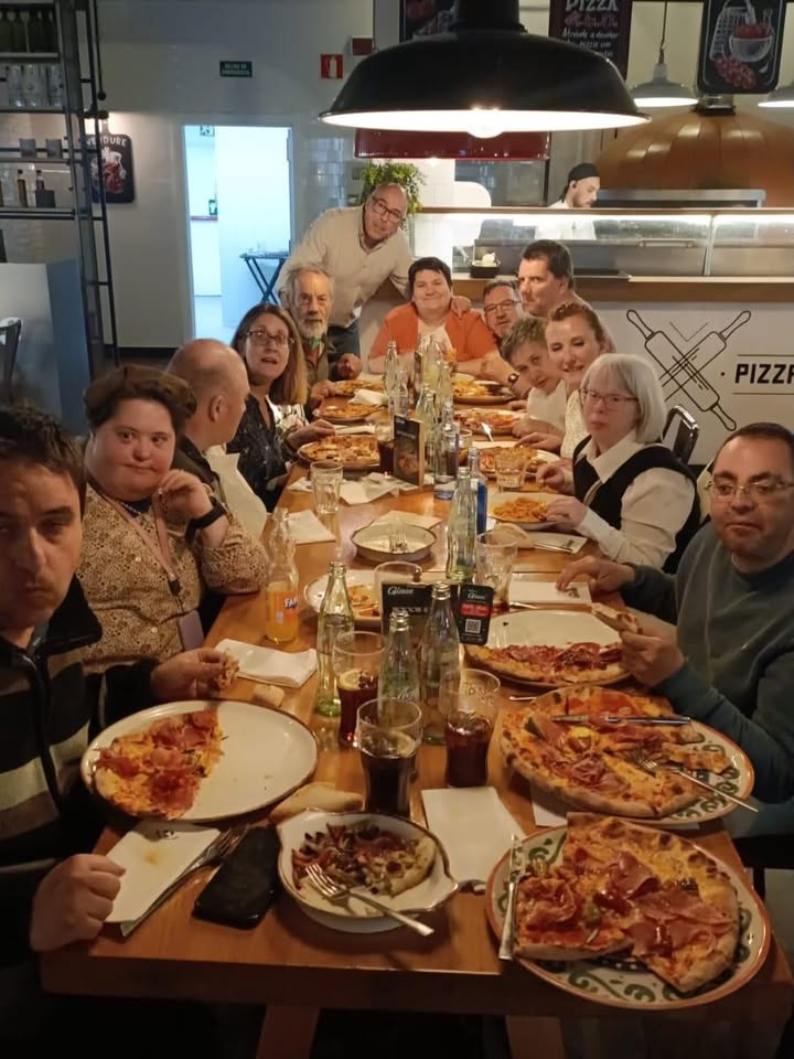 Grupo de personas disfrutando de una comida en una mesa con pizzas y bebidas