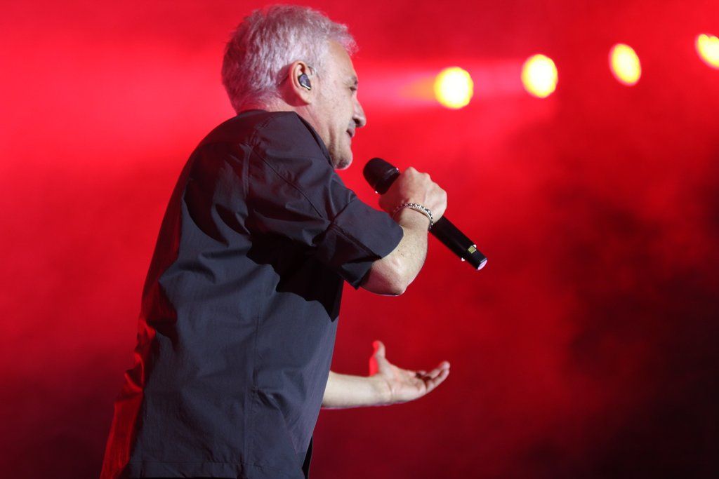 Sergio Dalma cantando en un concierto con luces rojas de fondo