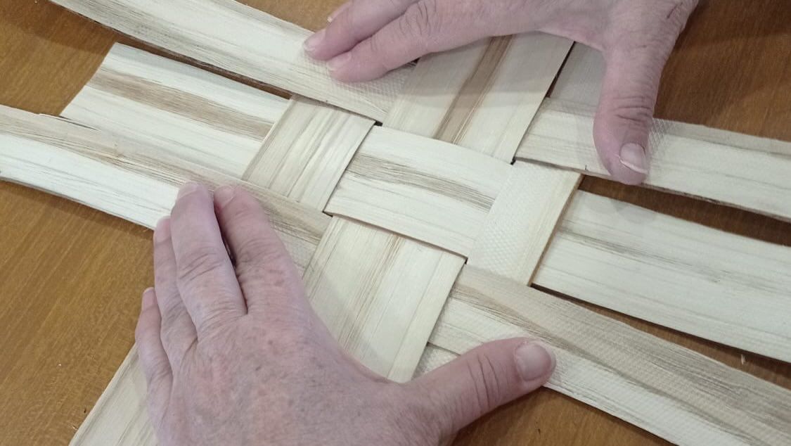 Manos tejiendo con mimbre en un taller de cestería