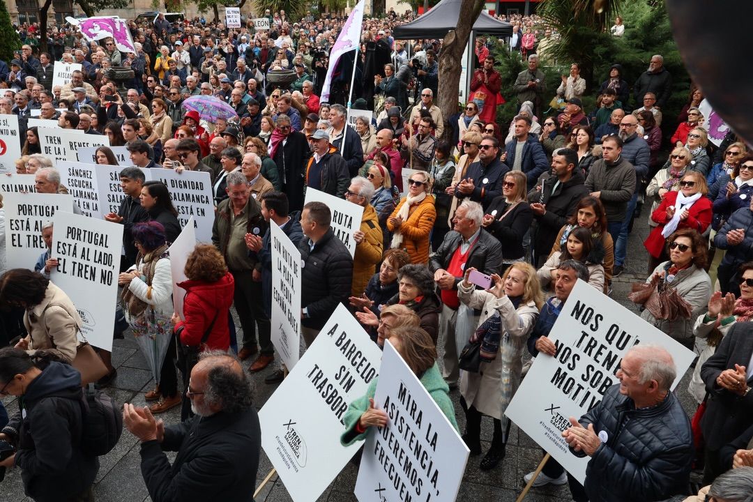Multitud de personas en la plaza de Los Bandos con pancartas sobre conexiones ferroviarias