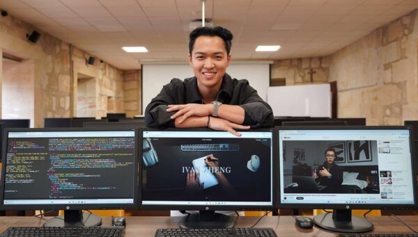 Estudiante Iván Zheng en un aula con computadoras mostrando código y proyectos