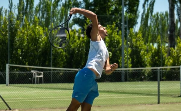 Joven jugador de tenis realizando un saque en un torneo deportivo