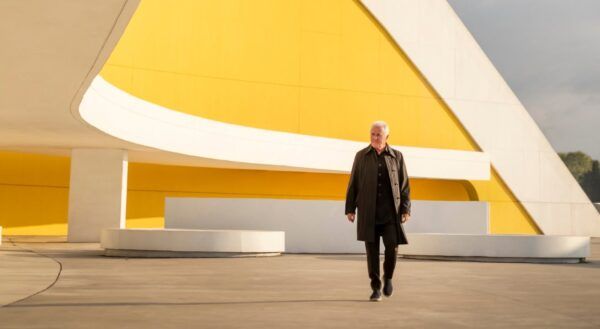 Víctor Manuel caminando frente a una estructura arquitectónica moderna y colorida