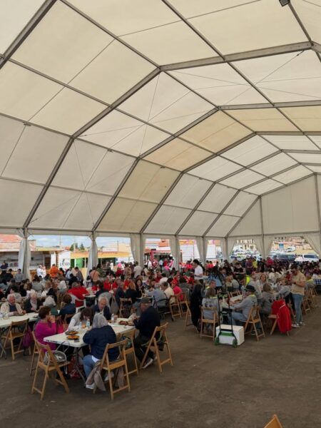 Gran cantidad de personas disfrutando de una comida solidaria bajo una carpa en Villamayor.