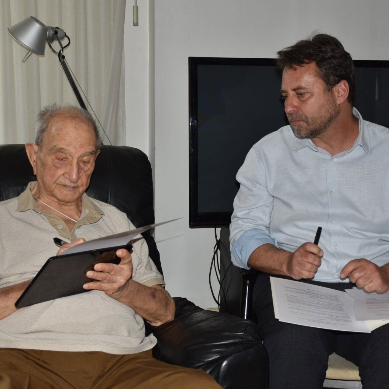 Dos hombres discutiendo sobre la capa de Claudio Sánchez-Albornoz en un ambiente acogedor.