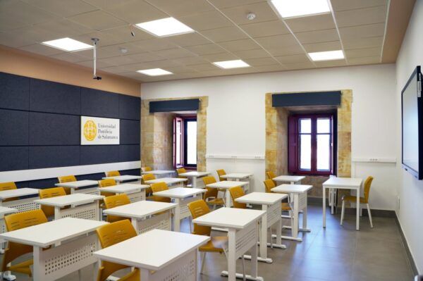 Aula moderna en la Universidad Pontificia de Salamanca con mesas y sillas amarillas.
