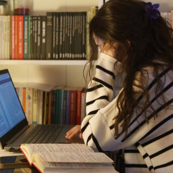Estudiante concentrada en su computadora con libros de fondo