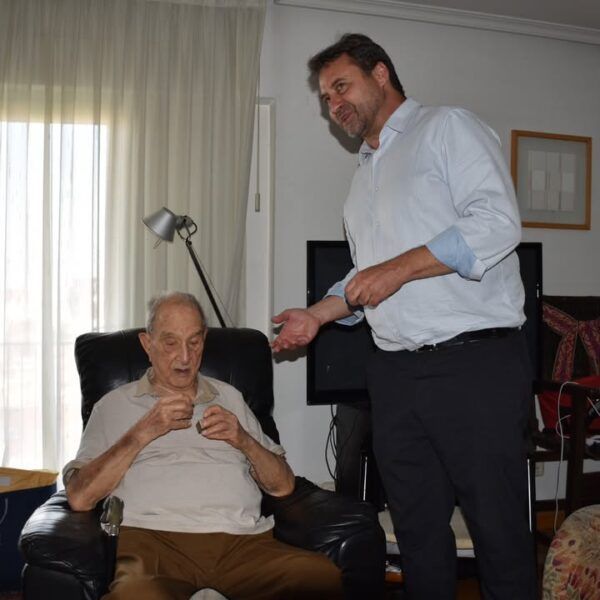 Dos hombres conversando sobre una capa histórica en un entorno doméstico.