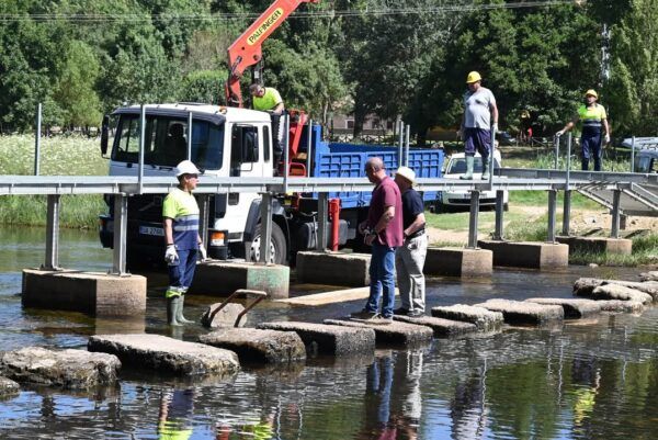 Trabajadores supervisando la instalación de una pasarela peatonal sobre el río Águeda.