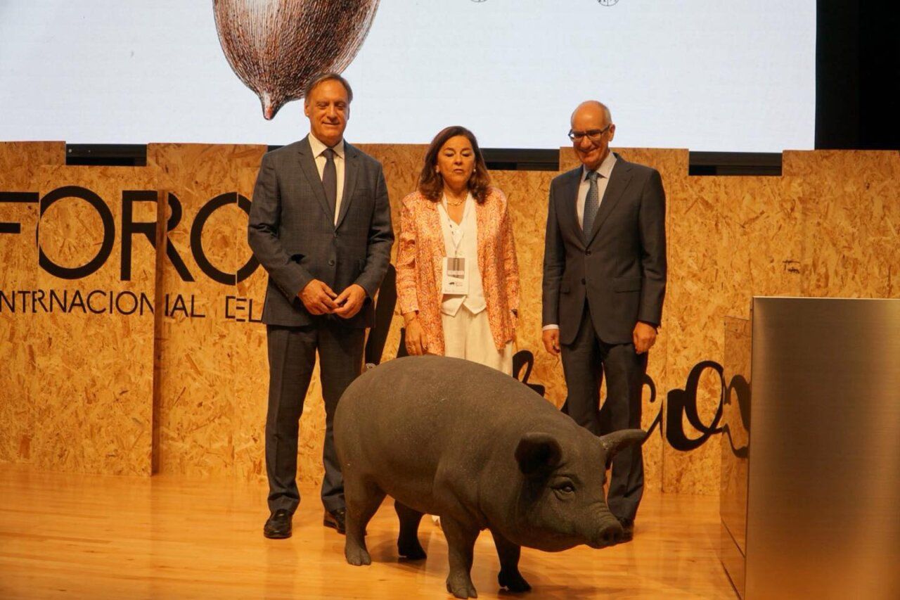 Tres personas posando junto a una escultura de cerdo en un evento gastronómico.